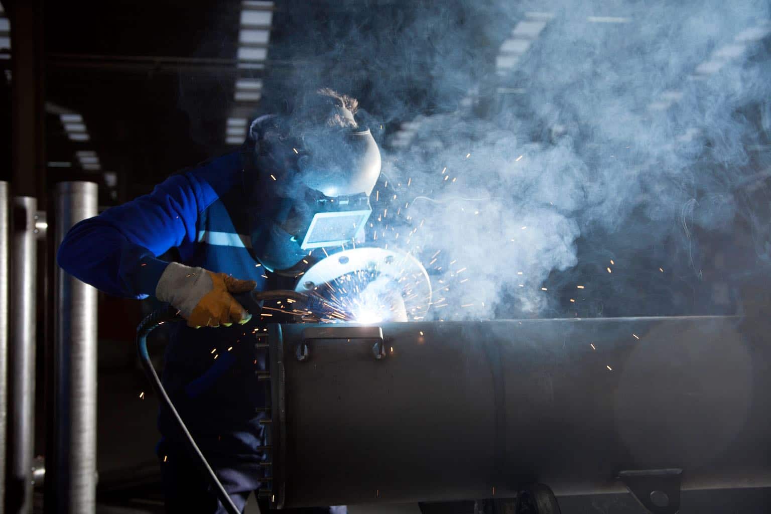 Refinery worker welding in darkness illuminated by sparks