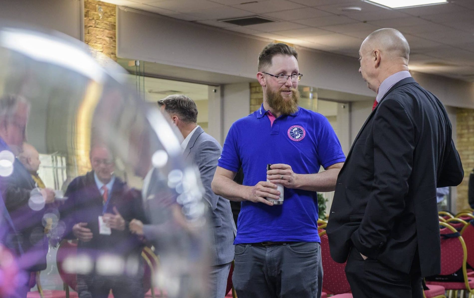 Plasma ball in the foreground (left) with two men stood in conversation in background (right)