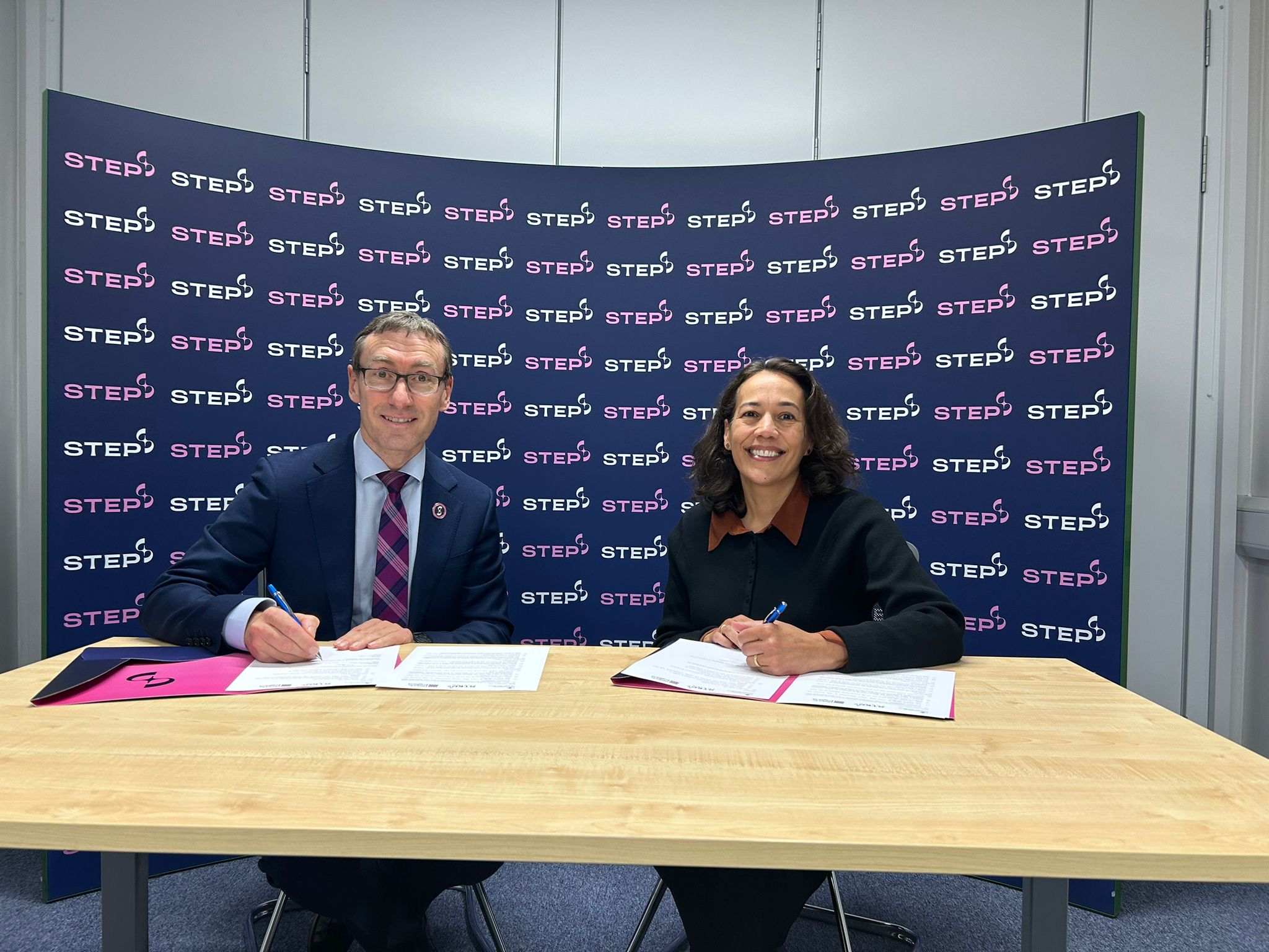 Paul Methven and Claudia Kenyatta sign the MoU documents in front of a STEP branded background.
